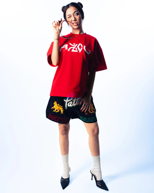 Person wearing a red oversized shirt with branding and a black skirt with yellow design on a white background
